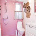 Bathroom with pink walls, toilet, shower, and sink with mirror cabinet.