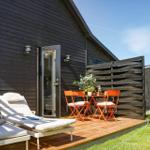 Deck with loungers and orange table set in front of a dark wood house.