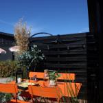 Orange table and chairs on terrace with plants and background house.
