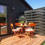 Terrace with orange table and chairs, plant and table decor. Wooden wall and glass door.