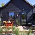 Black wooden house with terrace, orange table and chairs, seating areas, and plants.