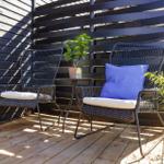 Deck with two chairs, table, and plant against dark wooden wall.