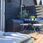 Deck with blue table and chairs, sun lounger, and plants in front of dark wood house.