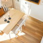 Dining area with wooden table, chairs, and candles. Window sill with plant and cushions.