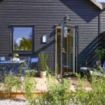 Terrace with table, chairs, and seating area in front of a house with dark wooden facade.