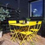 Outdoor area with yellow table and chairs, plants, and window on black wall.