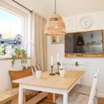 Dining area with wooden table, chairs, and window seat. Wall clock and TV are visible.