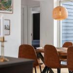 Esstisch mit braunen Stühlen und hängender Lampe. Wandbilder und Fenster mit Außenansicht.