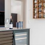 Küchenbereich mit Wein, Gläsern und Kaffeetassenregal an der Wand.