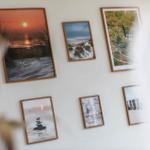 Wand mit sechs gerahmten Fotos von Küstenlandschaften und einem Leuchtturm.
