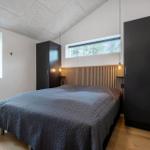 Schlafzimmer mit Bett, zwei Fenstern und zwei schwarzen Schränken.