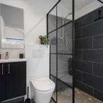 Badezimmer mit Dusche, Waschbecken und Toilette. Schwarze Fliesen und Spiegelschrank.