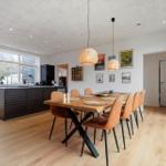 Esszimmer mit Holztisch, orangefarbenen Stühlen und moderner Küchenzeile.