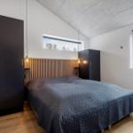 Schlafzimmer mit Bett, Kleiderschränken und Fenstern. Holzfußboden und schräger Deckenbereich.