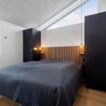 Schlafzimmer mit Doppelbett, Holzfußboden und großen Fenstern. Zwei schwarze Schränke und Holzpaneelen an der Wand.