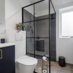 Badezimmer mit Dusche, Waschbecken und Toilette. Schwarze Fliesen und goldene Griffbügel.
