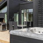 Außenbereich mit Whirlpool, Grill und Sitzgruppe vor einem modernen Haus.