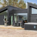 Moderne Holzhütte mit Terrasse, Grill und Whirlpool im Freien.