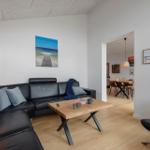 Wohnzimmer mit schwarzer Ledercouch, Holztisch und Wandbild. Durchgang zur Essnische.