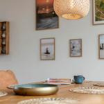 Esszimmer mit Holztisch, Stühlen und Wandbildern. Deckenleuchte und Tischmatte sichtbar.