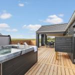 Terrasse mit Whirlpool und Sitzbereich. Holzdecke und schwarze Fassade. Blick auf grüne Landschaft.
