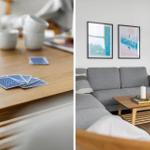 Holztisch mit Spielkarten und Tassen. Wohnzimmer mit grauem Sofa, Holzcoffee-Tisch und Wandbildern.