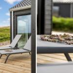 Zwei Liegestühle auf Holzterrasse vor modernem Haus mit Blick auf Grünland.