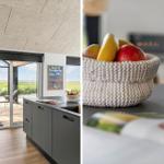 Küche mit Blick auf Terrasse und Landschaft. Obstschale auf Tisch. Holzboden und moderner Küchenbereich.