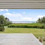 Deck with view of green field and lake under blue sky.