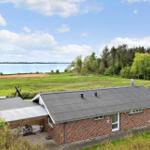 A red brick building with a gray roof, surrounded by green fields and a lake.
