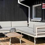Terrasse mit grauem Ecksofa und Holztisch. Hintergrund: schwarze Wand und Fenster.