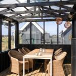 Terrasse mit Tisch, Stühlen und Feuerkamin. Glasdach und Sicht auf Umgebung.
