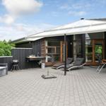 Terrasse mit Liegen, Grill und Sitzbank vor modernem Haus mit Glasfront.