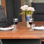 Holztisch mit zwei Platzsetzungen, Wein und Blumen auf der Terrasse.