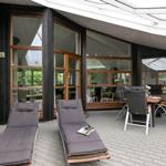 Terrasse mit Liegen und Tisch. Durchgehende Glaswände. Holzrahmen. Dachkonstruktion.
