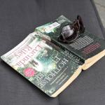 Ein Buch mit Sonnenbrille darauf liegt auf einer dunklen Außentischplatte.