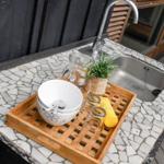 Außenbereich mit Waschbecken, Mosaikarbeitsplatte und Holztablett mit Geschirr.