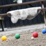 Fünf bunte Bälle liegen auf dem Boden vor einer Bank mit Decke.
