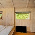 Bedroom with wooden walls, bed, TV, and two windows with view of greenery.