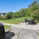 Terrace with table, chairs, and covered grill. Background: lawn and trees.
