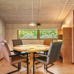 Dining room with round table and four chairs, wooden walls, windows with view of greenery.