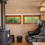 Room with wooden walls, wood stove, and leather recliner by windows with green view.