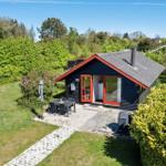 Modern wooden cabin with garden, terrace, and grill area. Surrounded by greenery and trees.