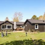 Ein dunkles Holzhaus mit Terrasse und Garten. Umgeben von Bäumen unter blauem Himmel.