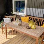 Holzterrasse mit Tisch, Stühlen und Kissen. Fenster und Hängedekoration sind sichtbar.