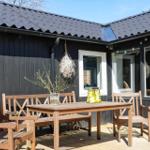 Holzterrasse mit Tisch und Stühlen vor schwarzem Haus mit Dach und Fenstern.