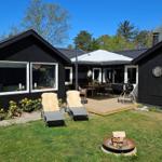 Schwarze Holzhütte mit Terrasse, Liegestühlen und Grill. Feuerkorb und Dartscheibe im Garten.