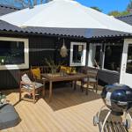 Terrasse mit Tisch, Stühlen, Sonnenschirm und Grill. Holzdecke und schwarze Fassade.