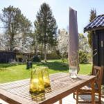 Holztisch mit zwei Stühlen auf Terrasse. Hintergrund: Grasfläche, Bäume und dunkle Holzhäuser.