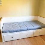 Ein weißes Bett mit drei Schubladen und einem grauen Matratzenbezug.